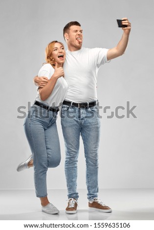 relationships, technology and people concept - portrait of happy couple in white t-shirts taking selfie smartphone by over grey background
