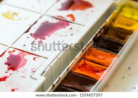 Watercolor palette. An artist mixes colors on a palette. Red paint on a white palette. Plastic box with paints.