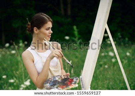 woman model on white canvas paints a picture in a clearing