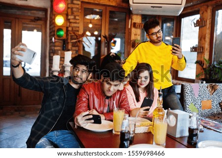 Group of asian friends sitting cafe. Happy indian people having fun together, sitting on couch and making selfie at mobile phones.