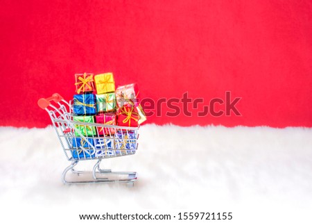 A shopping cart with presents in the snow in front of a red background