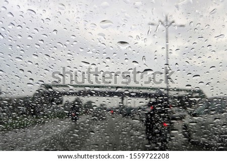 Road view through front car window mirror with rain. A drops of rain on car's mirror upon traffic road background.