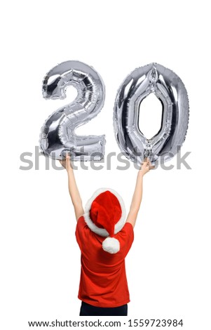 Boy in Santa hat holds up silver inflatable digit twenty. Back view. Isolated on white background.