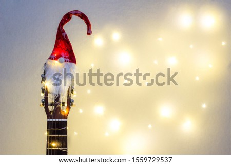 Acoustic Guitar with red Santa hat and light garland. Christmas music song concept with copyspace on white background