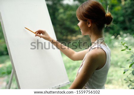 young woman outdoors an easel with white canvas