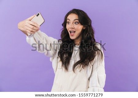 Image of positive surprised cute young brunette woman posing isolated over purple wall background take a selfie by mobile phone.