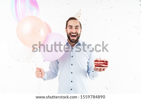Image of delighted party man laughing and holding birthday cake with air balloons isolated over white background