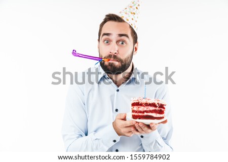 Image of positive man blowing party horn and holding birthday cake with candle isolated over white background
