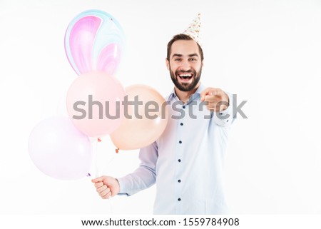 Image of pleased party man holding air balloons and pointing finger at you isolated over white background