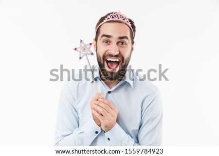 Image of happy girlish man wearing princess crown smiling and holding magical wand isolated over white background