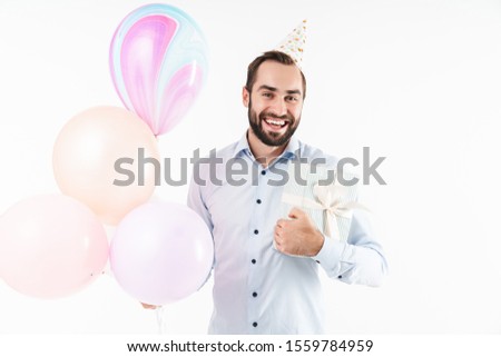 Image of happy party man smiling while holding air balloons and present box isolated over white background