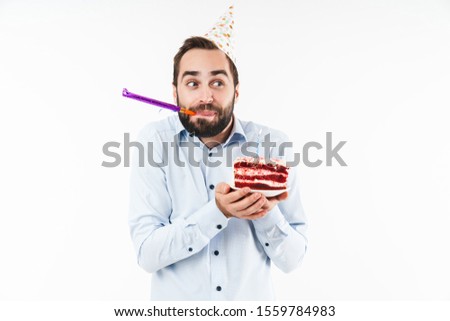 Image of joyful man blowing party horn and holding birthday cake with candle isolated over white background