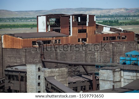 Old soviet unused outdated rusted factory building of metallurgy steel plant on the blue sky and mountains background. Taraz city, Kazakhstan