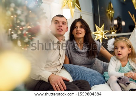 Happy family portrait on Christmas, mother, father and child sitting on bed at home, chritmas decoration around them