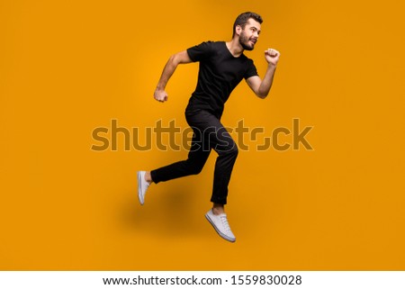 Full size photo of handsome millennial guy jumping high rush shopping mall black friday offers season fast wear black t-shirt trousers isolated yellow color background