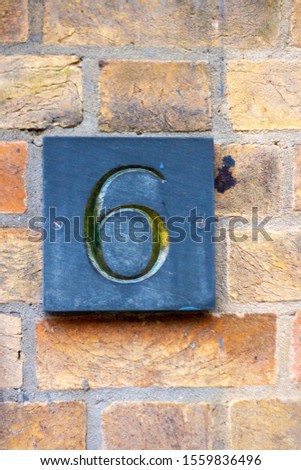 House number 6 carved in stone on a red brick wall