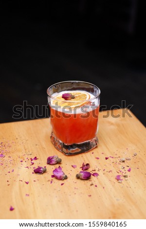 Red alcoholic cocktail decorated with rose flower and orange chips
