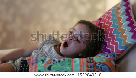 
Tired little child child yawning watching TV screen at home couch