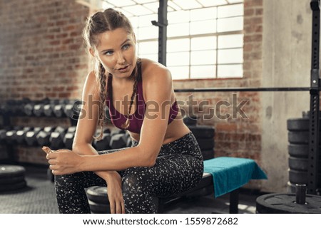 Sweaty young woman eating energy bar at gym after strong workout session. Beautiful exhausted woman enjoying chocolate bar after a heavy workout in fitness gym. Tired girl sitting with copy space Royalty-Free Stock Photo #1559872682