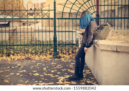 Emo girl smoking and use her phone in the street. Young student with blue colorful dyed hair