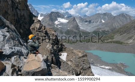 A mountain climber sitting at the pass takes picture of beautiful alpine landscape with photo camera. Upper stream of Kurkus river, Katun range, Altai, Russia.