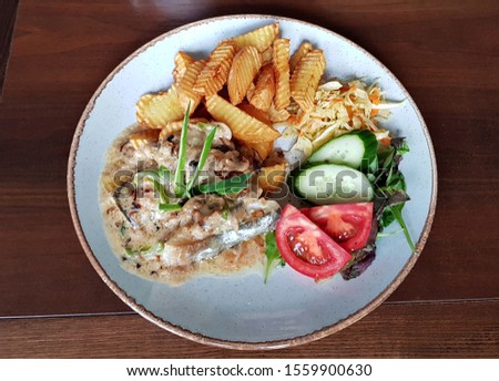Piece of pork with fried potatoes and mushroom sauce. Fresh vegetable salad on a white plate