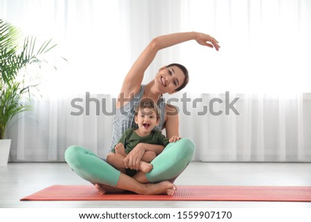 Young woman doing exercise with her son indoors. Home fitness Royalty-Free Stock Photo #1559907170