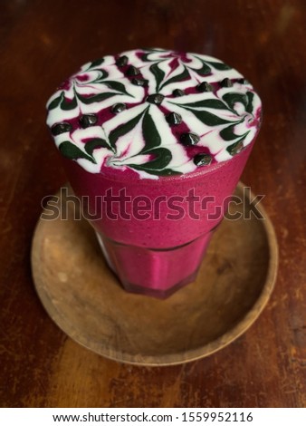 Healthy dragon fruit milkshake with a chocolate swirl pattern three quarter close up view on distressed wood surface.