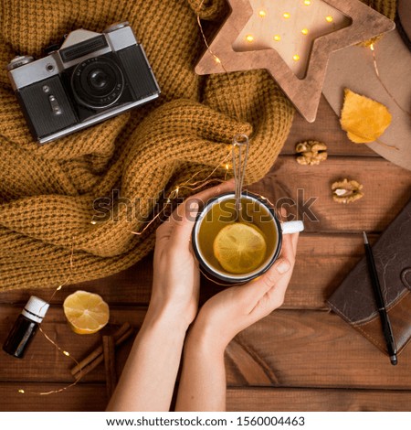 flat lay cozy autumn photo for a blogger with a warm sweater and hands holding tea with lemon, a retro camera and a wooden starry night light.