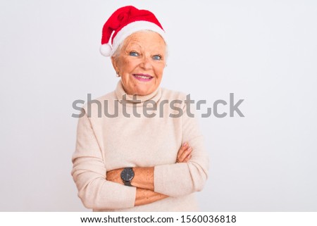 Senior grey-haired woman wearing Crhistmas Santa hat over isolated white background happy face smiling with crossed arms looking at the camera. Positive person.