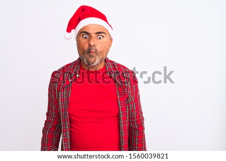 Middle age man wearing Christmas Santa hat standing over isolated white background making fish face with lips, crazy and comical gesture. Funny expression.
