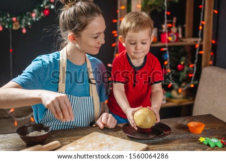 Mom and child son shape the dough for baking homemade holiday cookies on a dark background with garlands. Family cooking in Christmas decorations