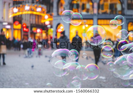 Selective focus of colourful of bubbles soap foam on the square of the Dam with blurred background of peoples walking around and Nieuwendijk street in the evening, Abstract background, Amsterdam.