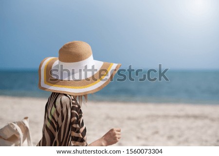 Young woman in sunhat relaxing on beach during summer vacation. She is against blue sea water on sunny day.