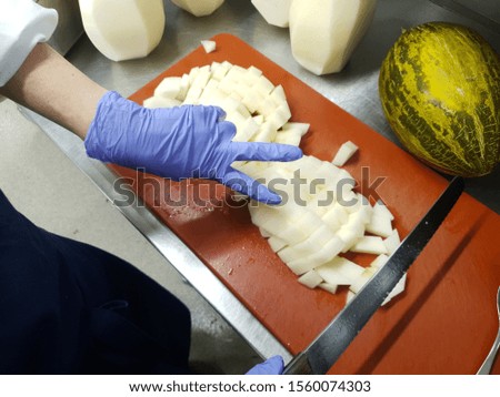 Young chef is cutting melon into cubes. In picture is professional kitchen environment.