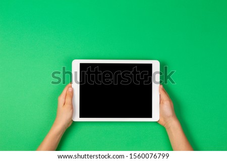 Child hands holding tablet computer on light green background