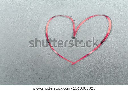 One beautiful bright red heart painted by finger on a frozen blue texture on a glass