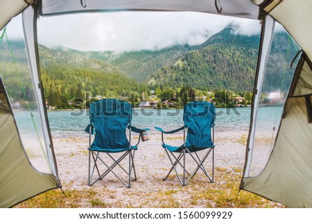 Inside tent. Romantic weekend in camping in Alps. Bavaria (Bayern), Germany. Furniture (chairs) on lake coast. Cozy happy morning together outdoor. Tourist photo. On mountain background.