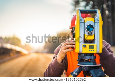 Surveyor engineer with equipment (theodolite or total positioning station) on the construction site of the road or building with construction machinery background Royalty-Free Stock Photo #1560102362