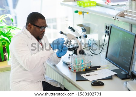 African-american scientist working in lab. Doctor making microbiology research. Laboratory tools: microscope, test tubes, equipment. Biotechnology, chemistry, bacteriology, virology and health care.
