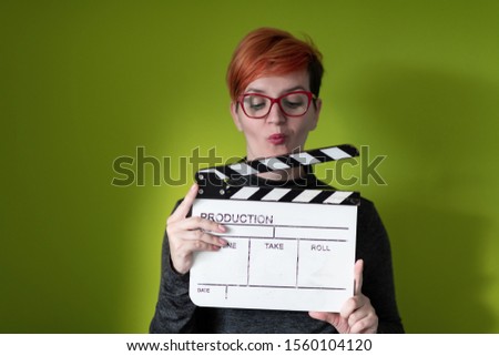 redhead woman holding movie clapper isolated against green background  cinema concept in studio