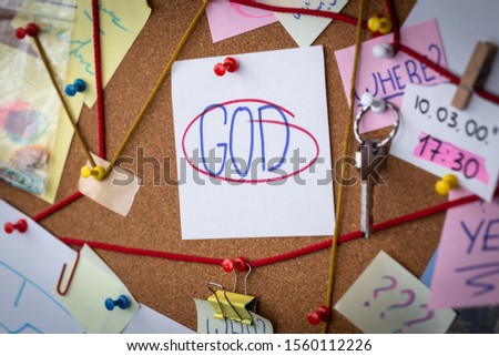 God search concept. Close-up view of a detective board with evidence. In the center is a white sheet attached with a red pin with the text God. Royalty-Free Stock Photo #1560112226