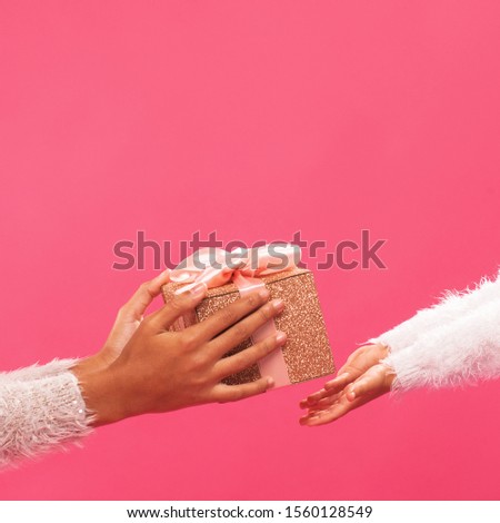 Closeup picture of giving and taking the gift box against vivid pink background