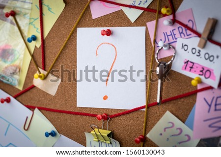 Question concept. Close-up view of a detective board with evidence. In the center is a white sheet attached with a red pin with the question symbol. Royalty-Free Stock Photo #1560130043