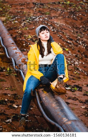 Young beautiful girl in yellow jacket sitting on pipeline at clay quarry, Lithuania.