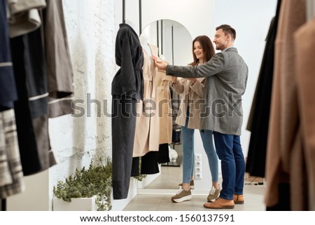 Smiling adult husband with wife checking price together and choosing clothes with sales and discount offer in shopping center