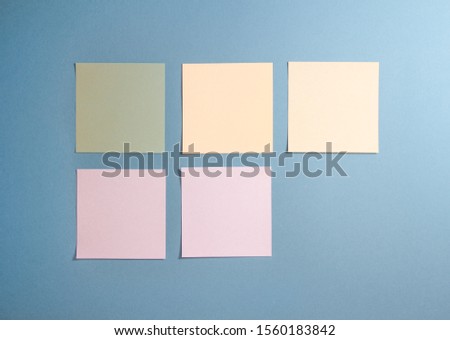5 blank white and pastel colors sticky notes on blue background, from top view