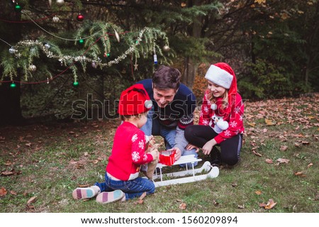 Father and two daughters open presents boxs near Christmas tree outdoor in the yard of the house.