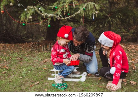 Father and two daughters open presents boxs near Christmas tree outdoor in the yard of the house.