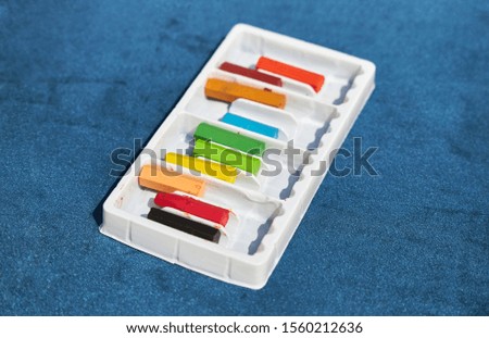 Set of colored crayons in a white box lies on a blue surface.